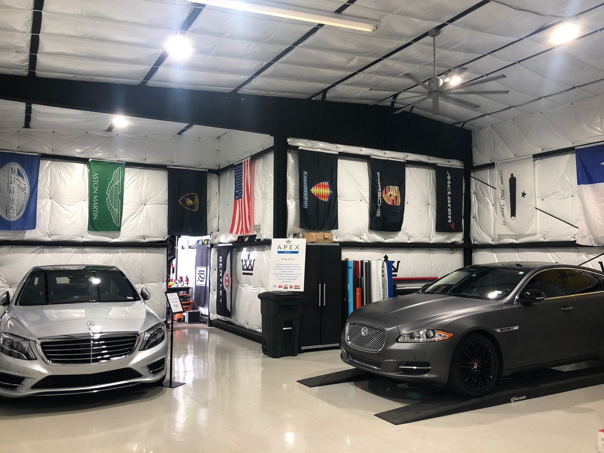 Two cars are parked in a garage with flags on the wall.