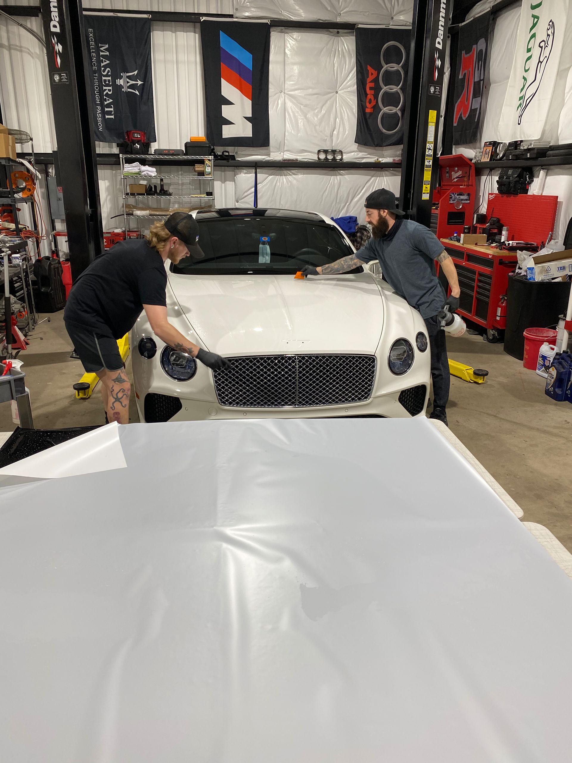 Two people applying film to a white Bentley in a garage.