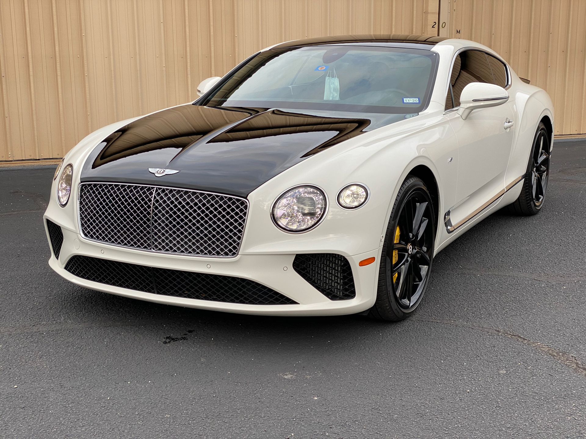 White Bentley coupe with a black hood parked on asphalt.