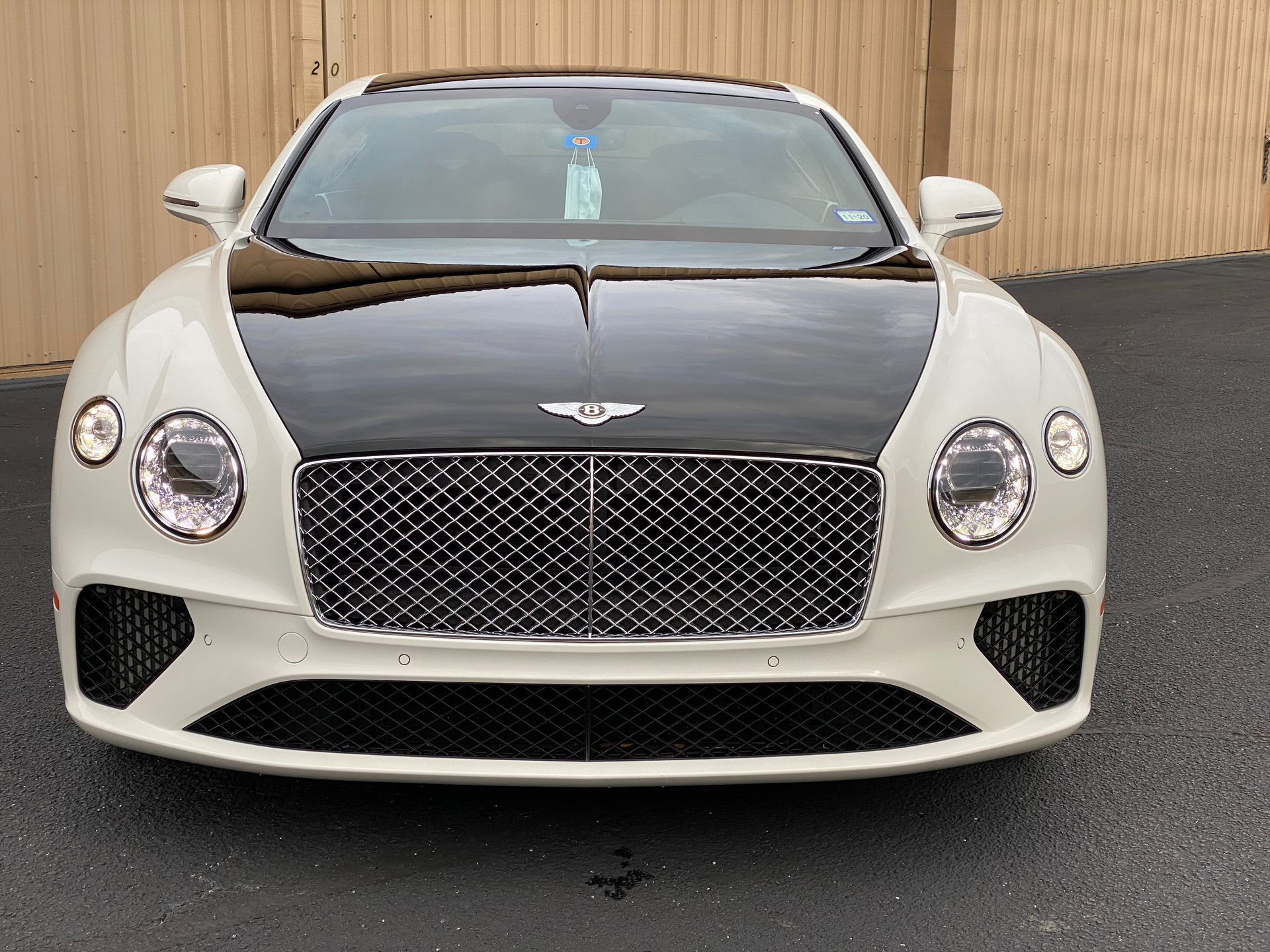 White Bentley coupe with black hood, parked on pavement.