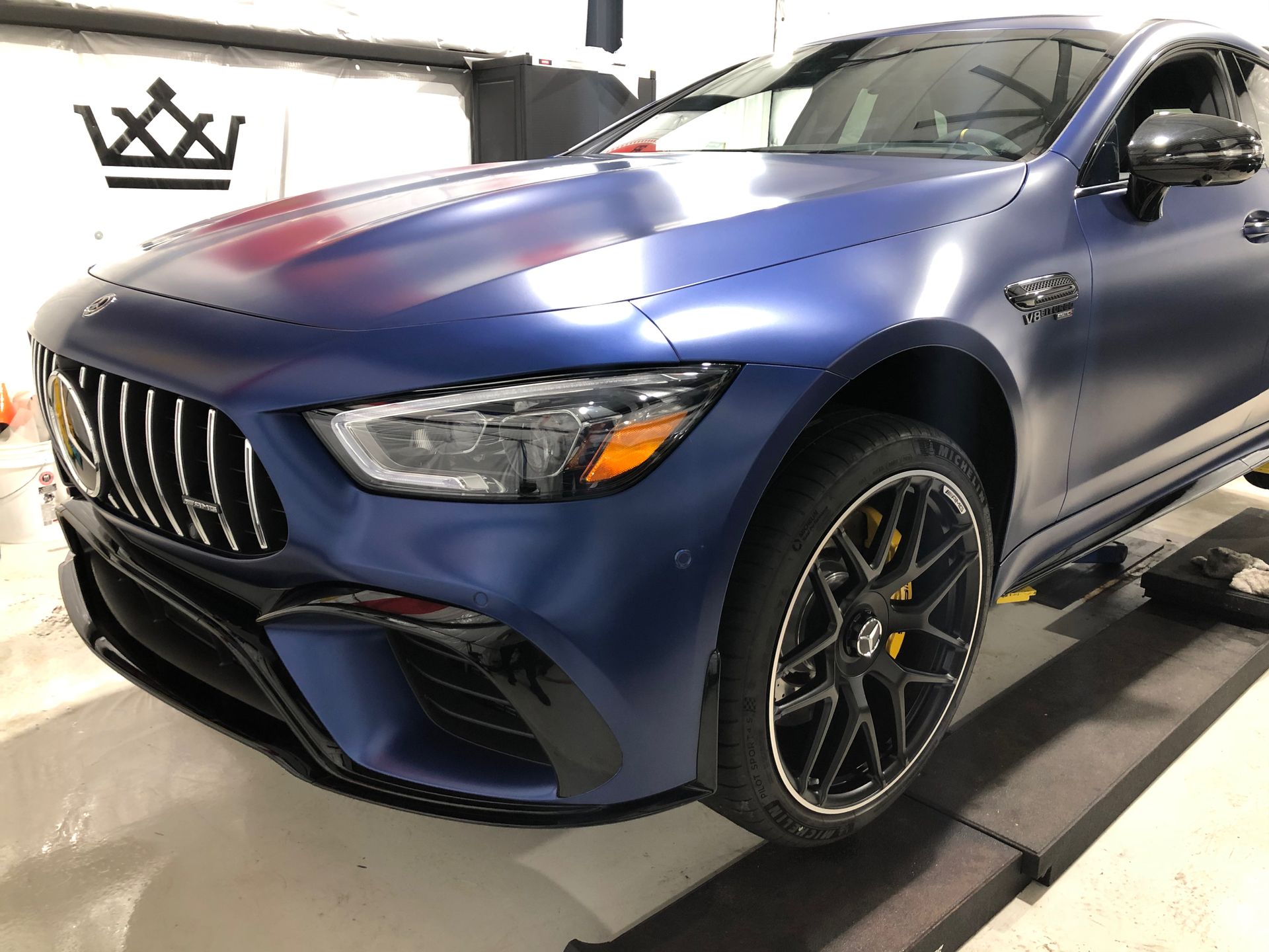 A blue mercedes amg gt63 coupe is parked on a lift in a garage.