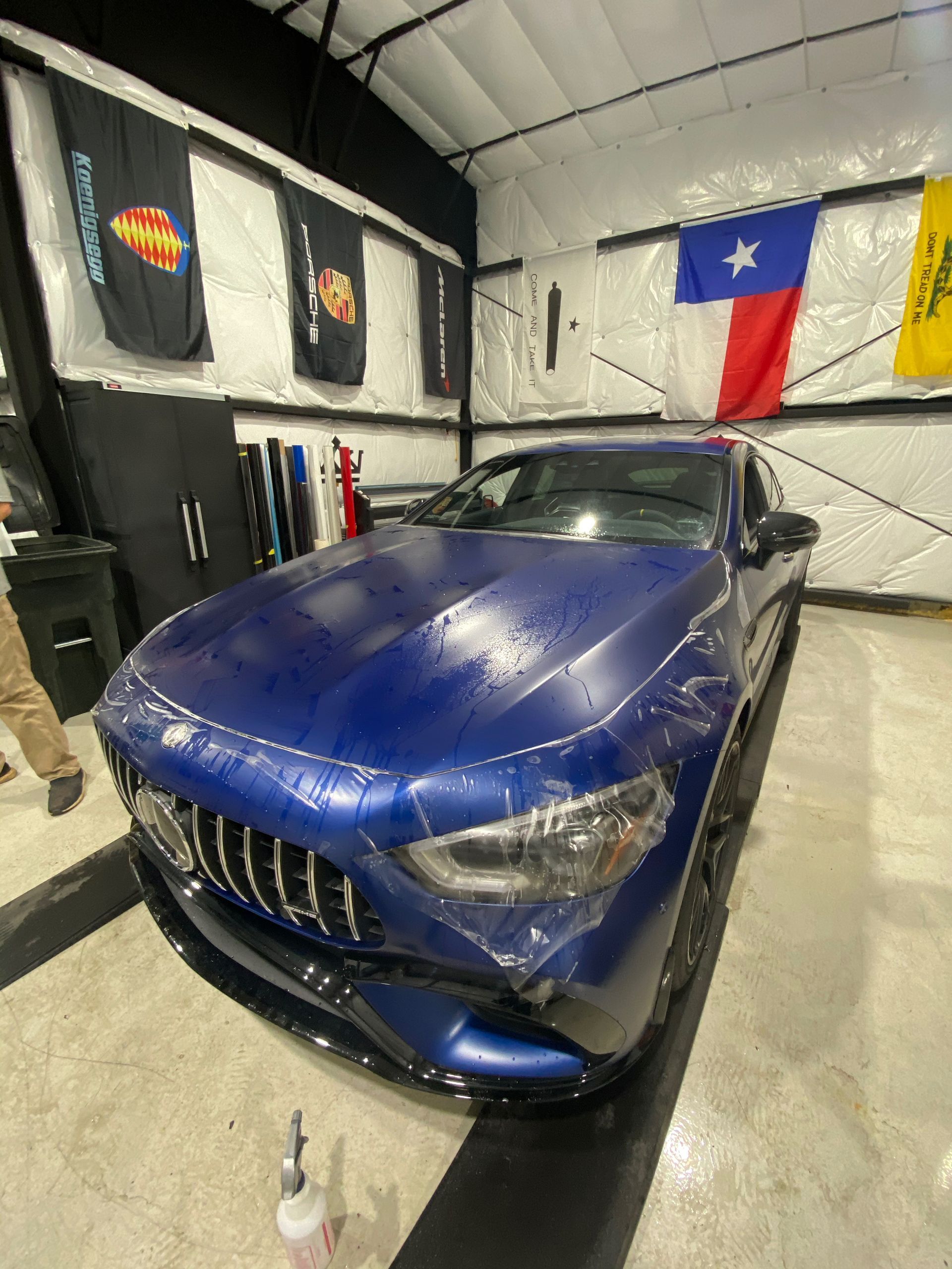 A blue car is parked in a garage with flags on the wall.