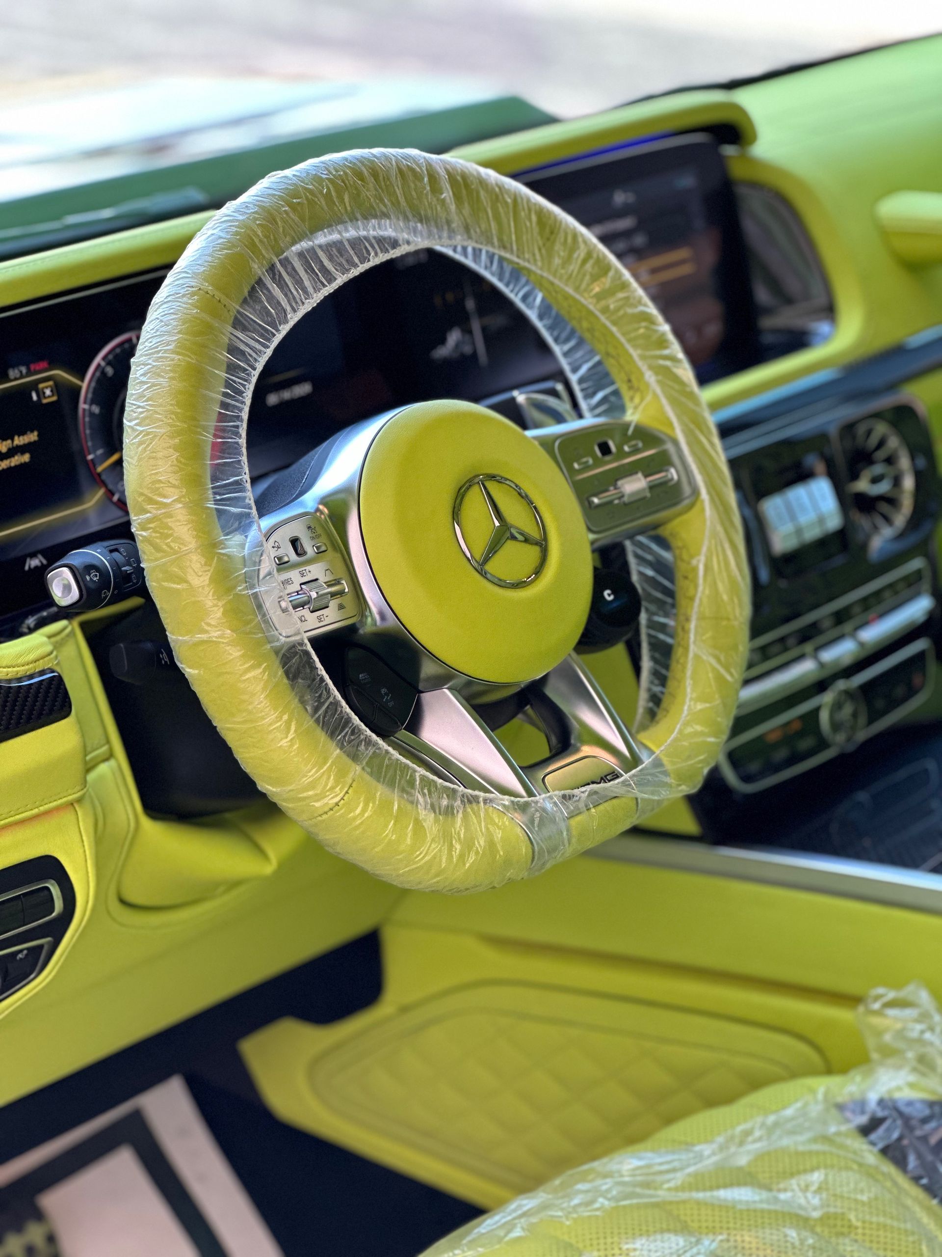Lime-green interior of a Mercedes-Benz, featuring a steering wheel in plastic wrap.