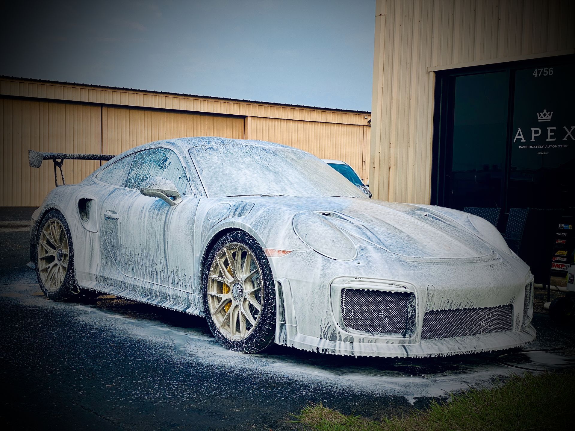 A white sports car covered in foam is parked in front of a building.
