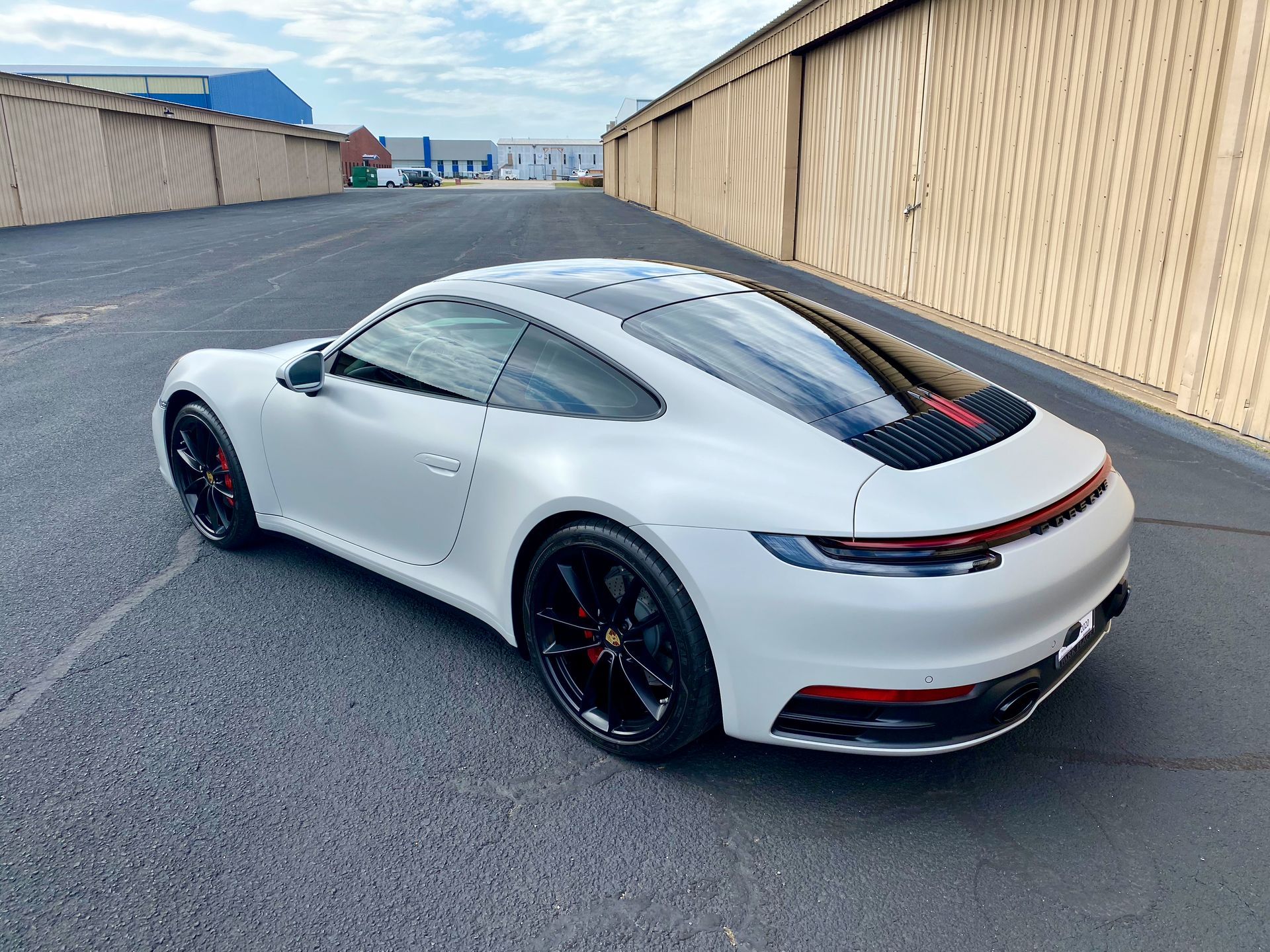 A white porsche 911 is parked in a parking lot.