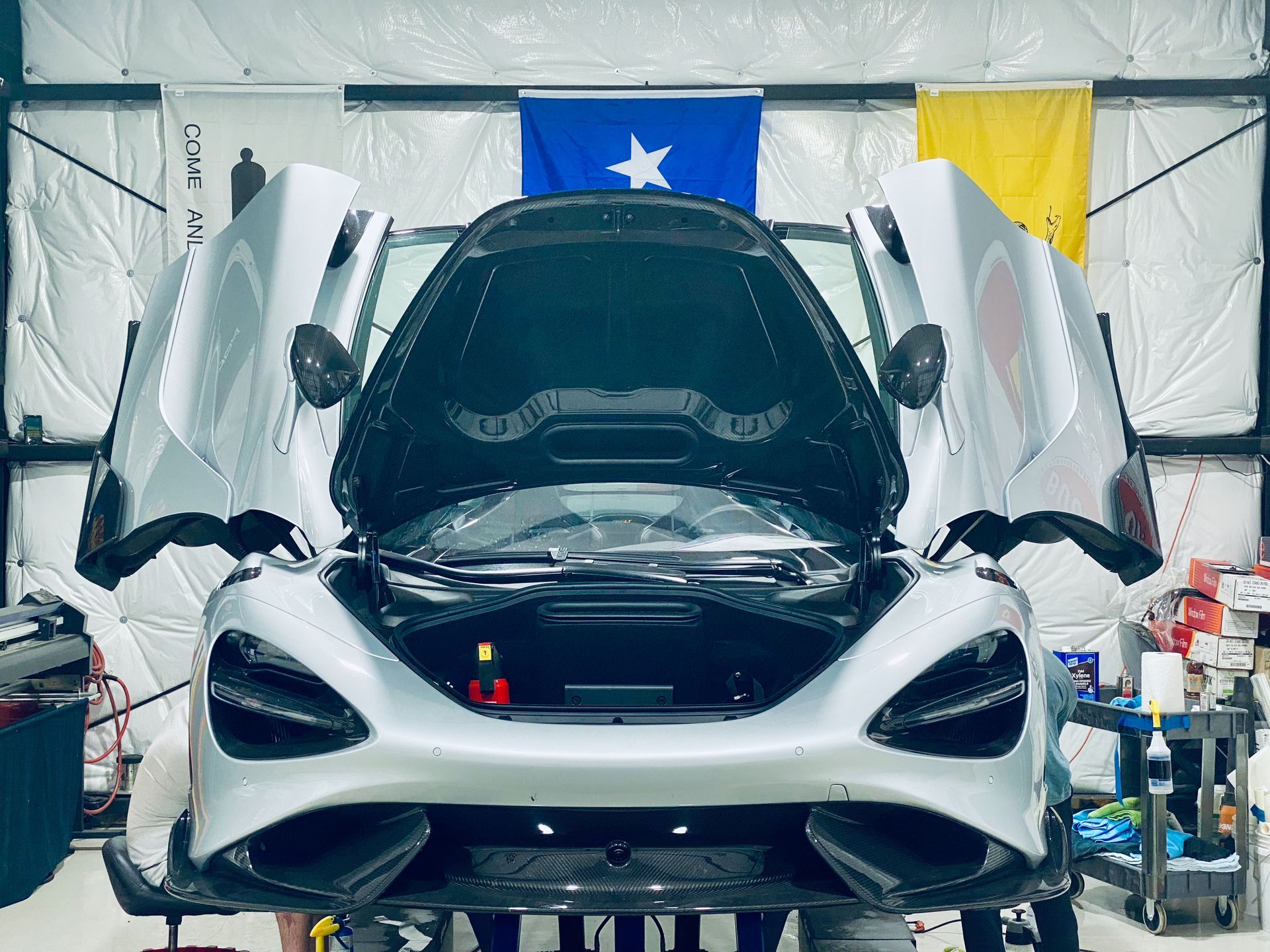 A silver sports car with its hood open in a garage