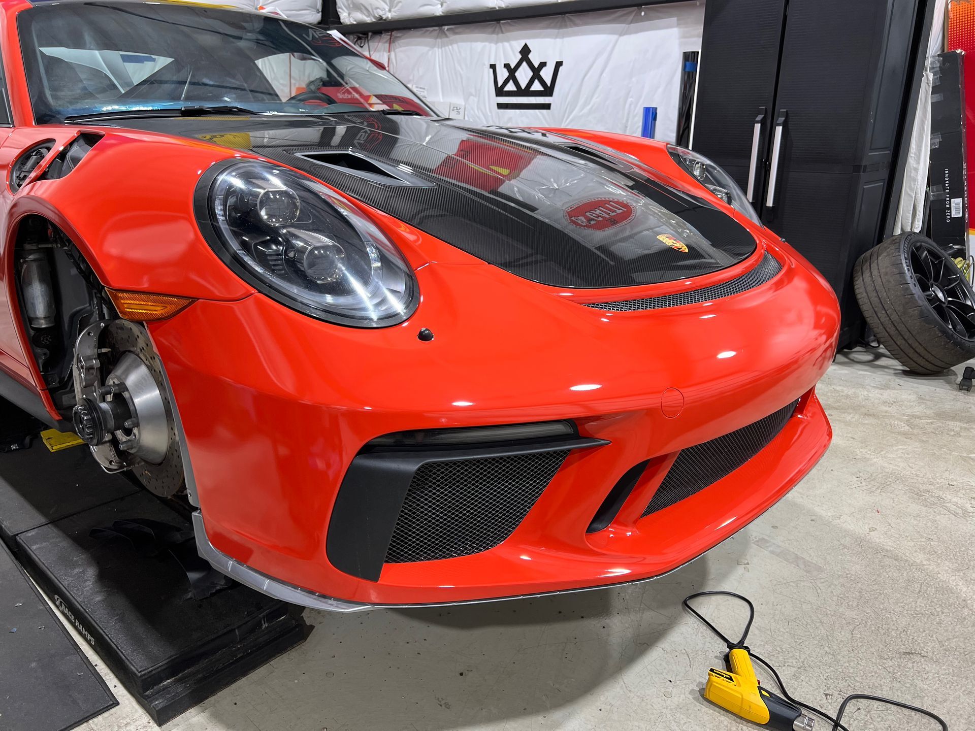 Red Porsche 911 GT3 in a garage with its front wheel removed and carbon fiber hood.