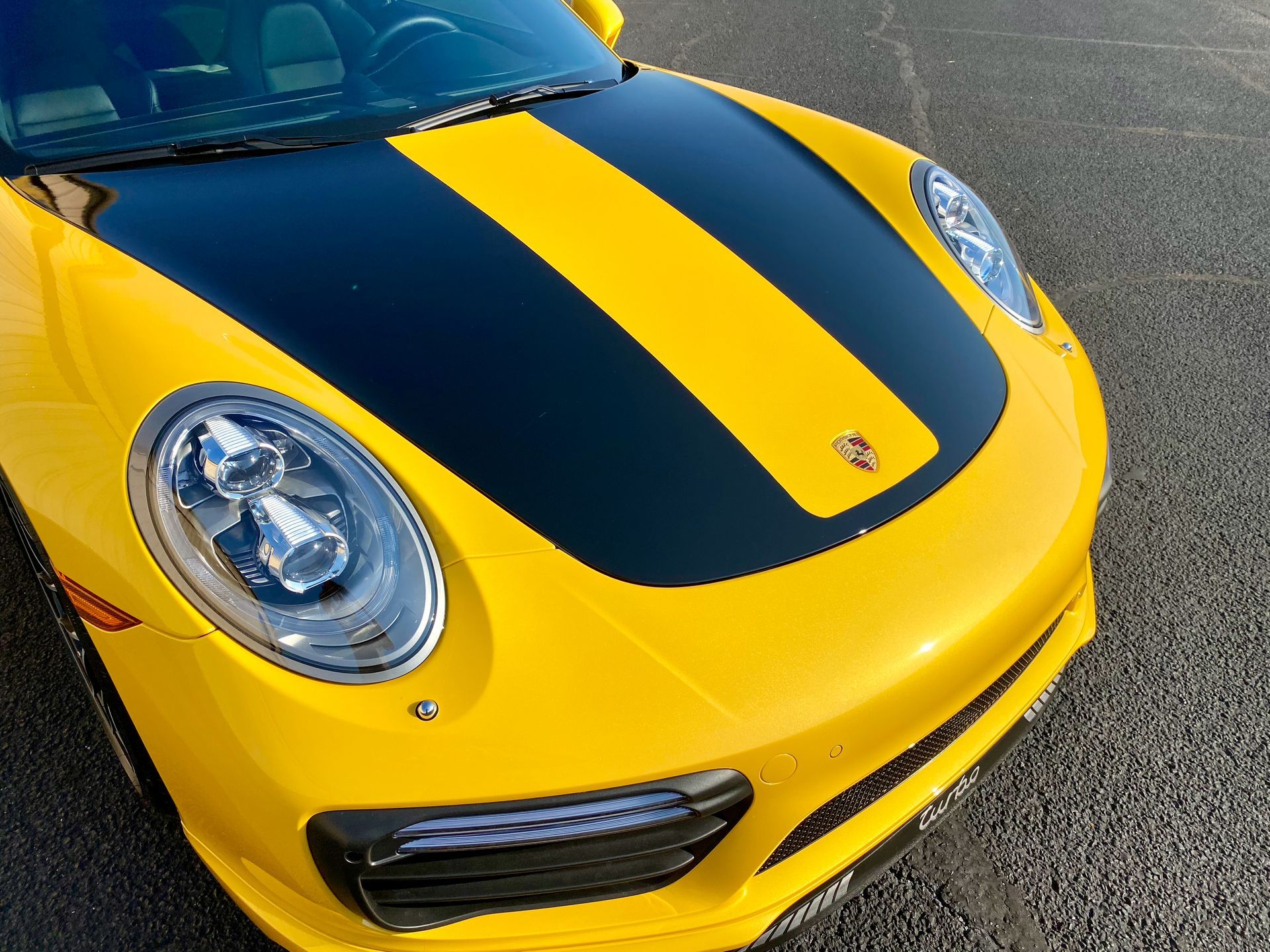 A yellow porsche with black stripes on the hood