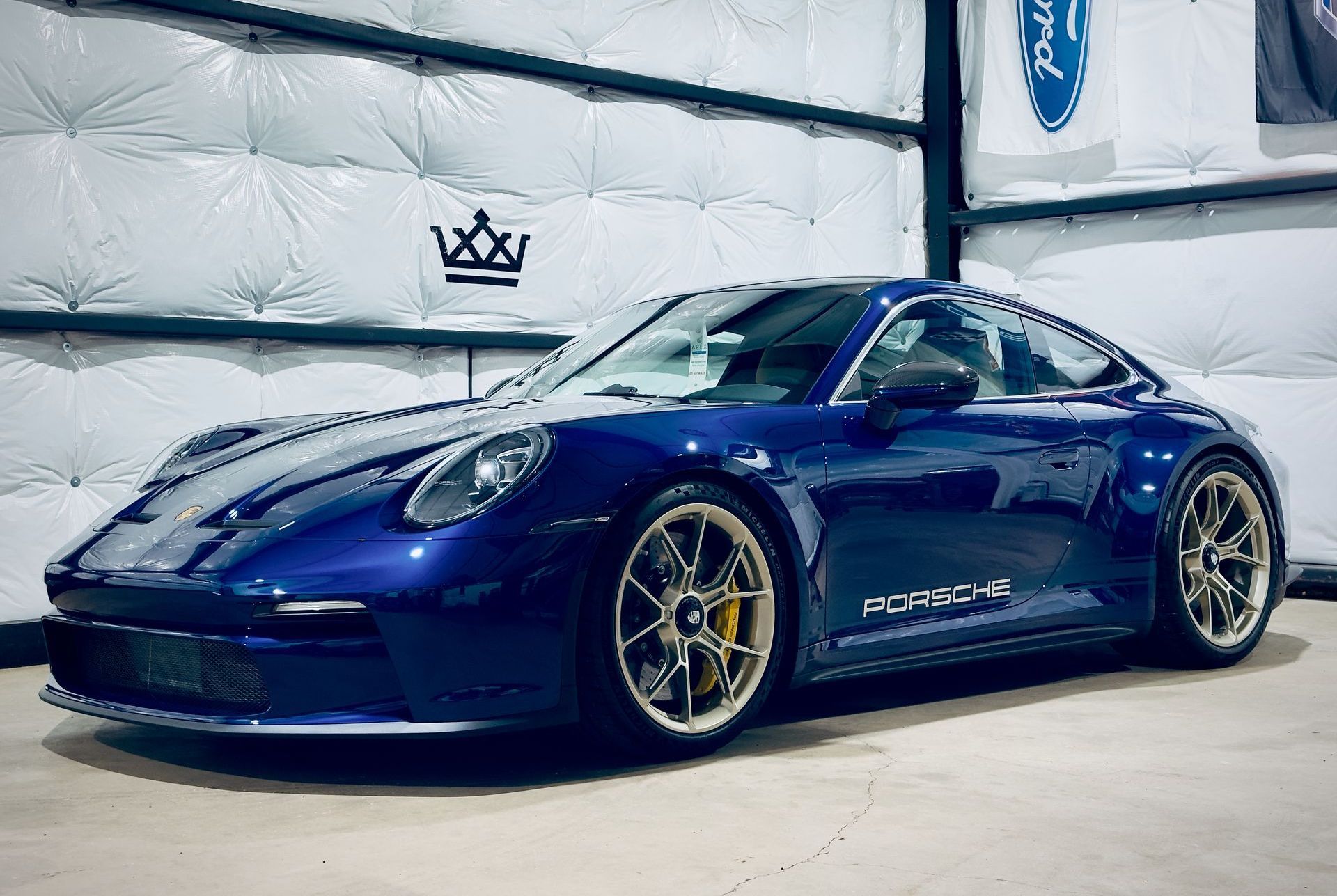A blue porsche 911 is parked in a garage next to a ford sign.