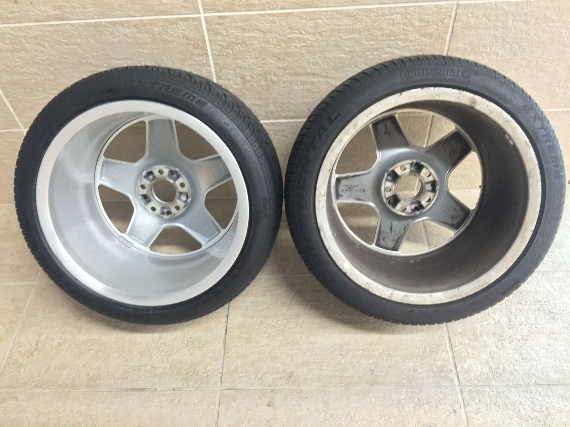 Two wheels and tires are sitting next to each other on a tiled floor.