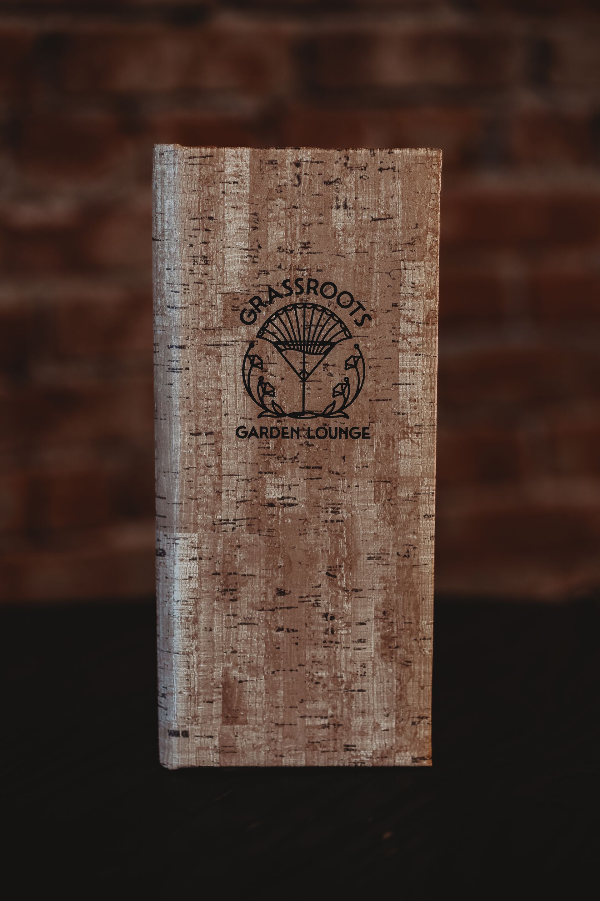 A cork wallet is sitting on a table in front of a brick wall.