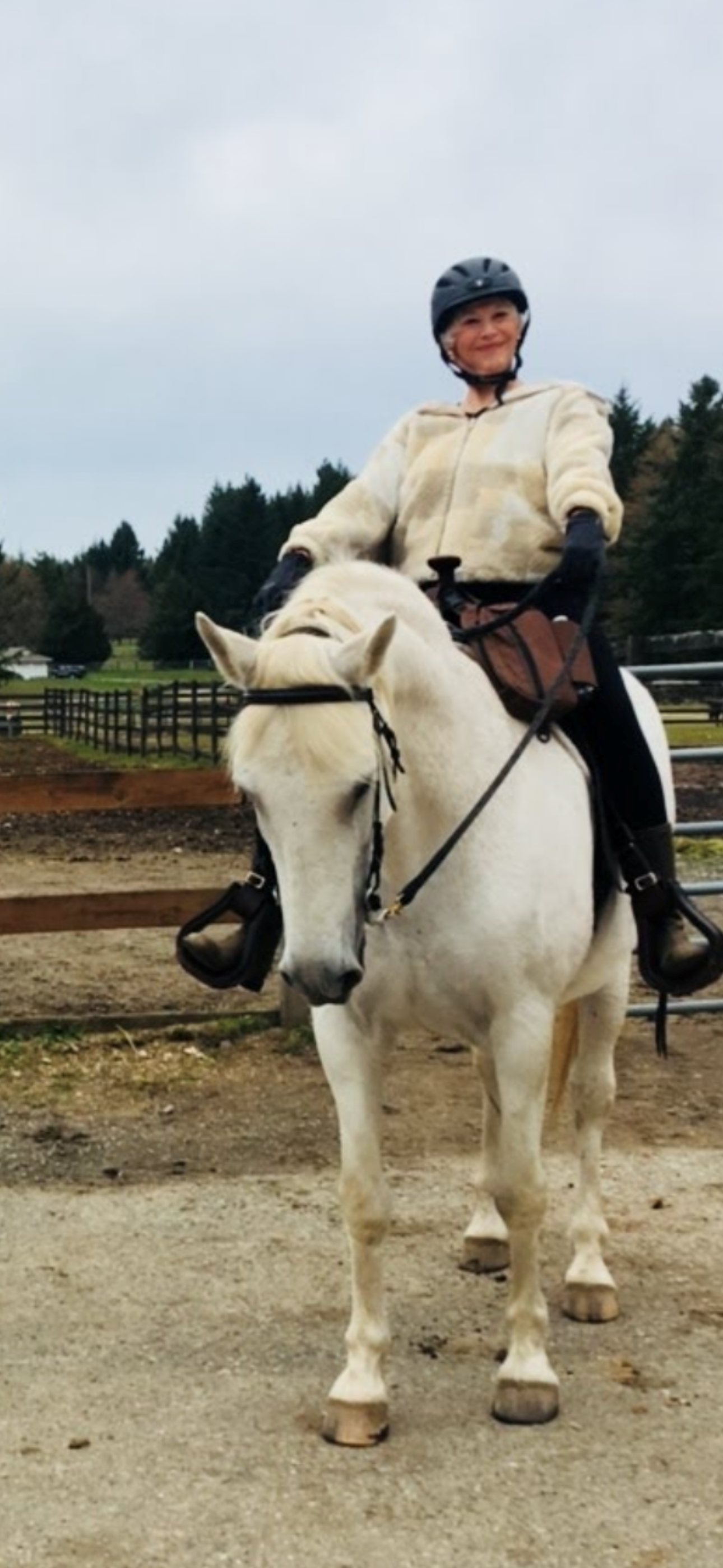A person wearing a helmet rides a white horse outdoors, smiling.