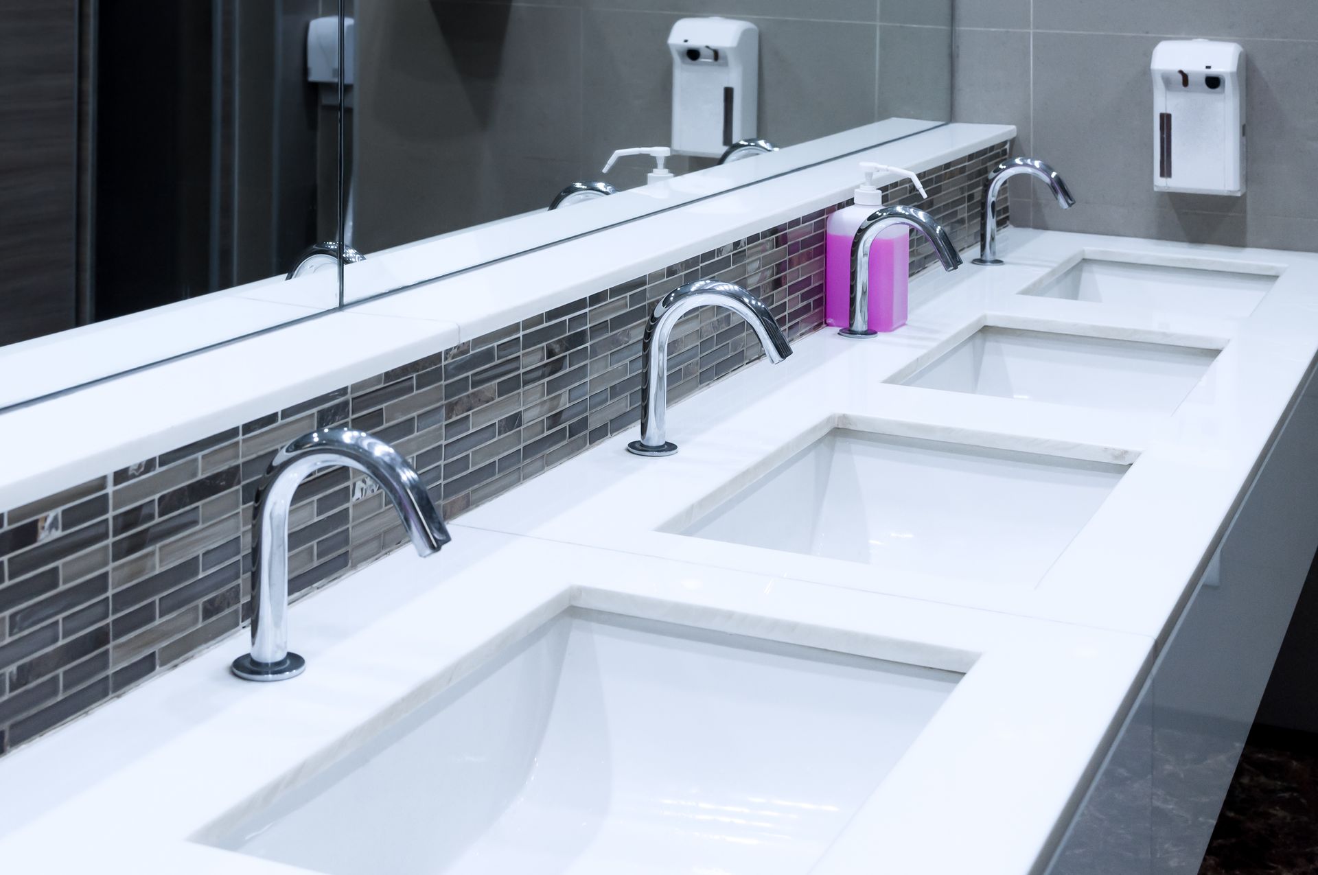 Modern public restroom sinks with chrome faucets, soap dispensers, and mirrors above countertops
