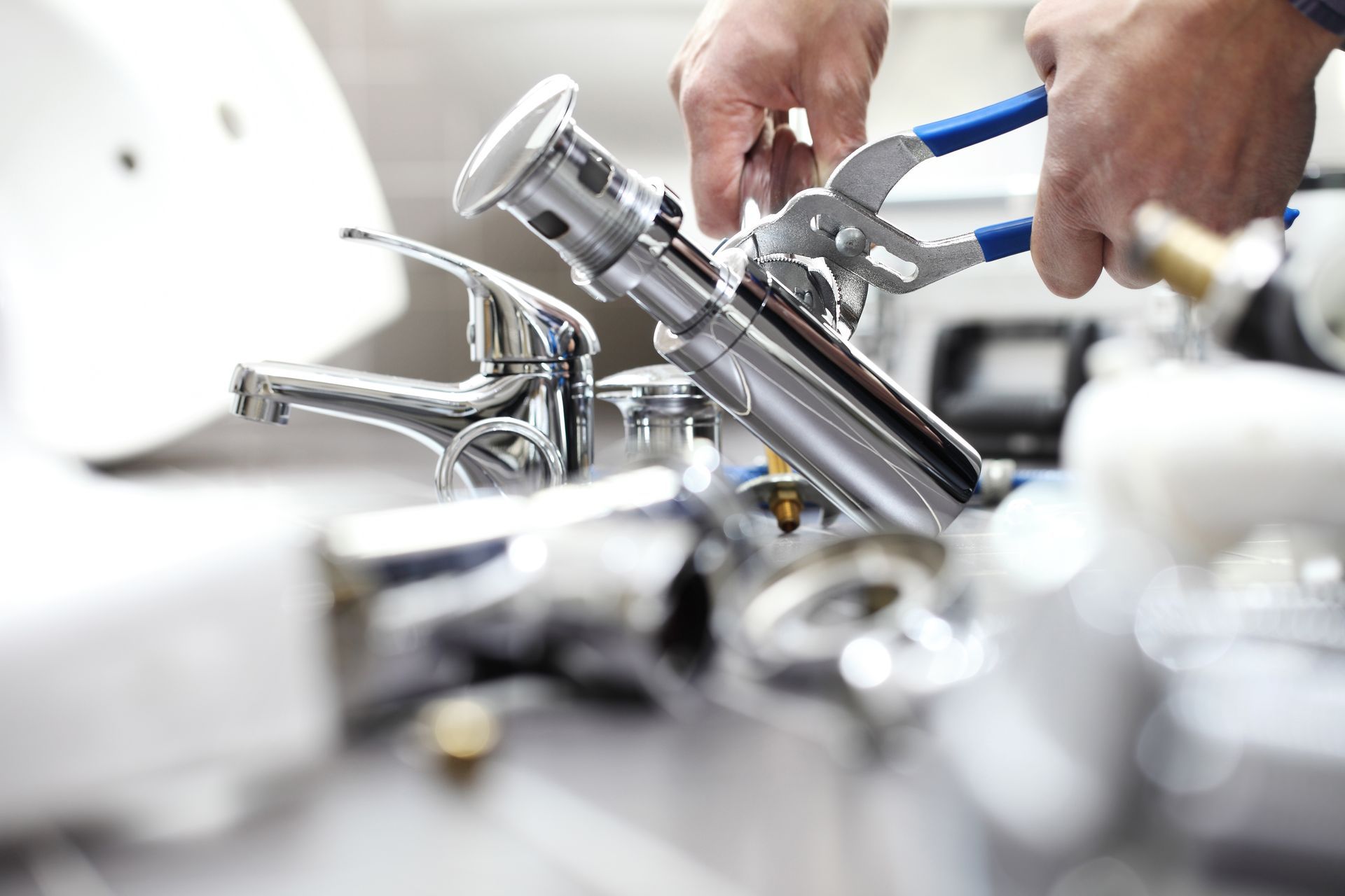 Hands using pliers to install a chrome sink drain and faucet on a bathroom sink.