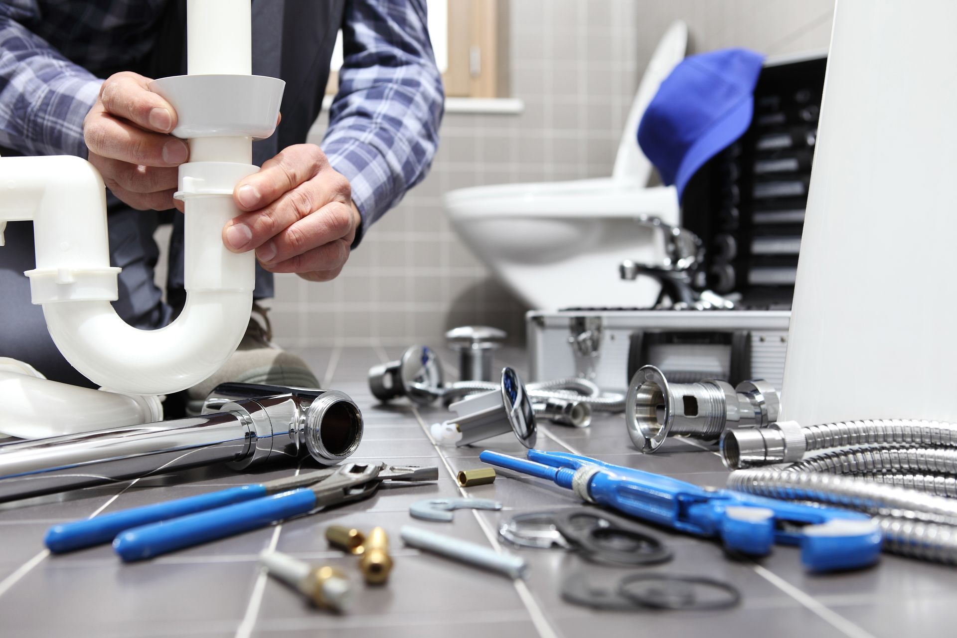 Plumber assembling PVC pipe fittings with wrenches and tools on a bathroom floor