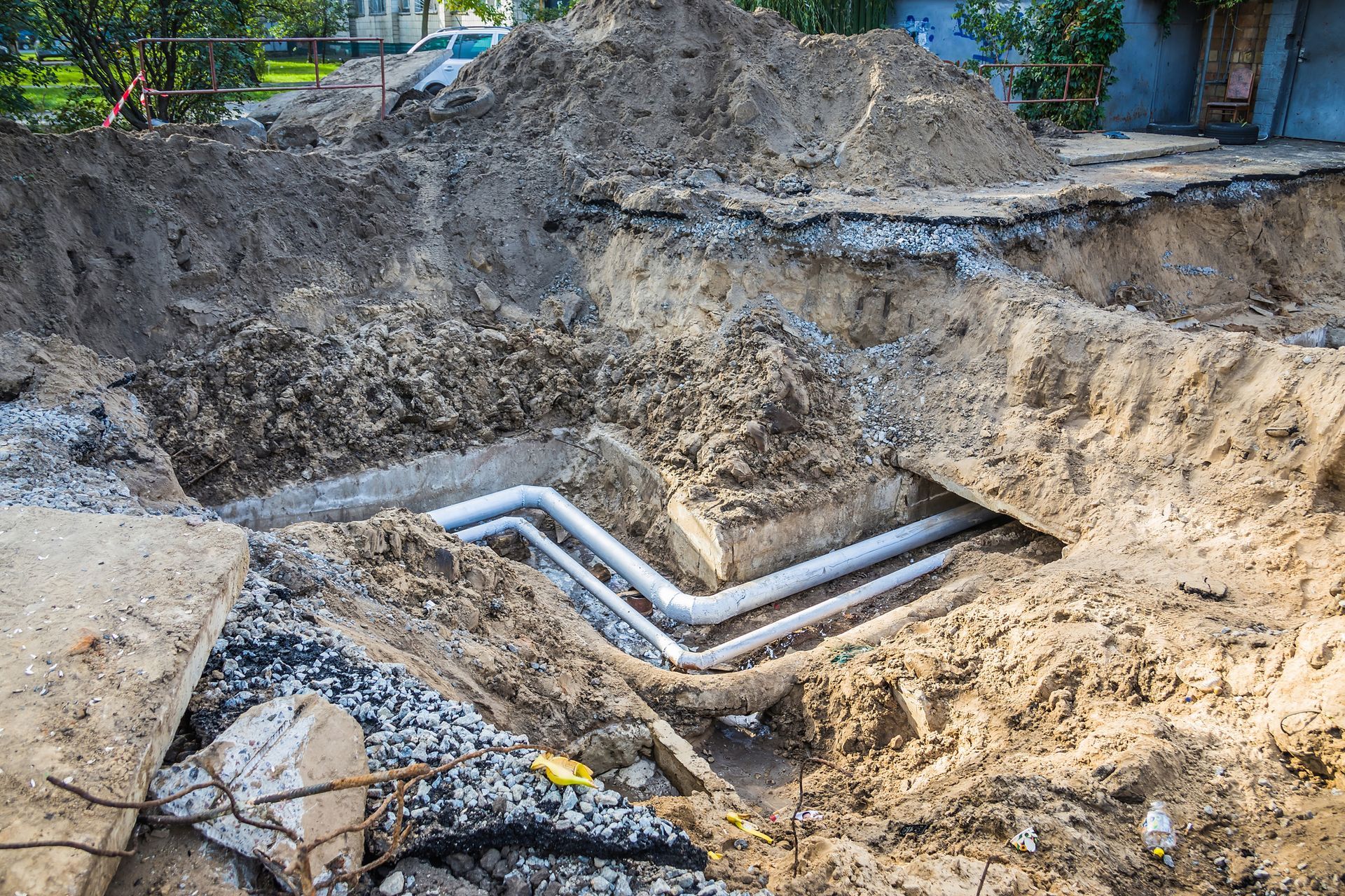 Construction site with buried white pipes in an open trench, surrounded by dirt and debris.