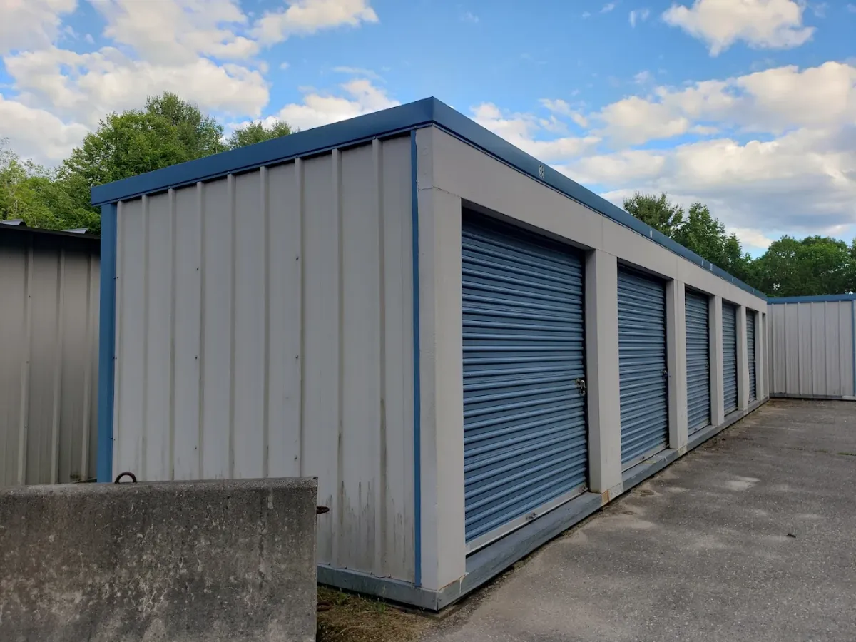Row of beige and blue storage units with roll-up doors, set against a blue sky and concrete ground.