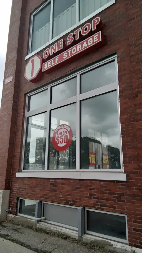 Exterior of "One Stop Self Storage" building with a sign above the window. A "$50 OFF" promotional sign is visible 