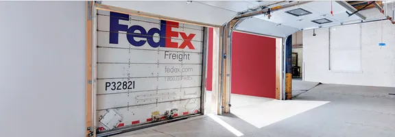 A wide shot of a warehouse interior with a FedEx-branded garage door that's partially open.