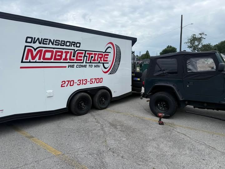 A black Jeep next to a trailer for Owensboro Mobile Tire in a parking lot.