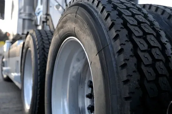 Truck tires, close-up, with black rubber treads on silver rims. Focus on tire detail and truck exterior.