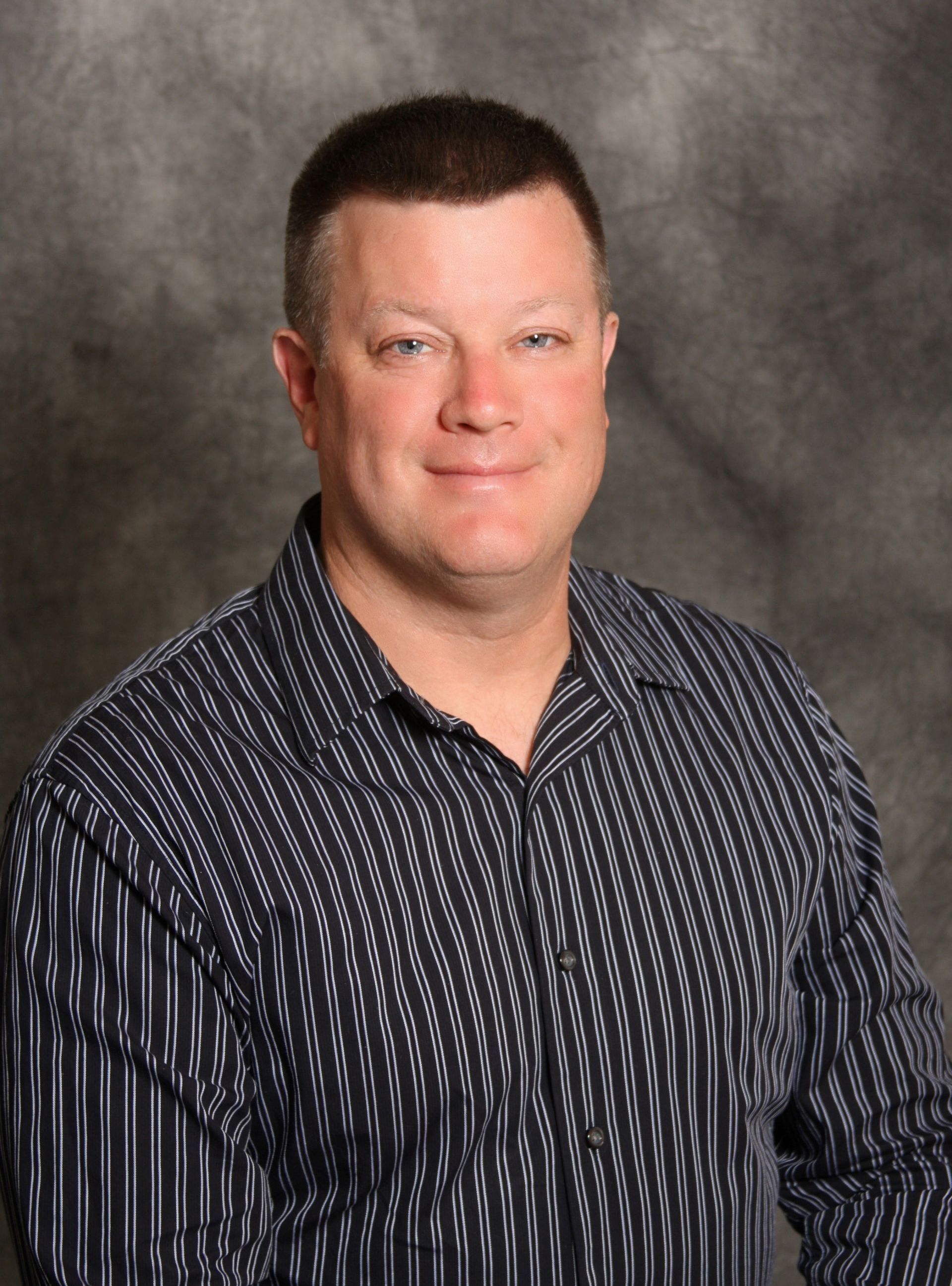 Man with short brown hair and a striped shirt smiling, studio shot.