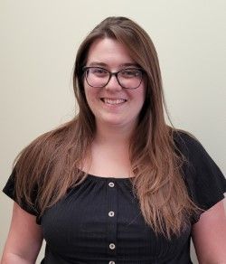 Woman with long brown hair, glasses, and a black top smiling at the camera.