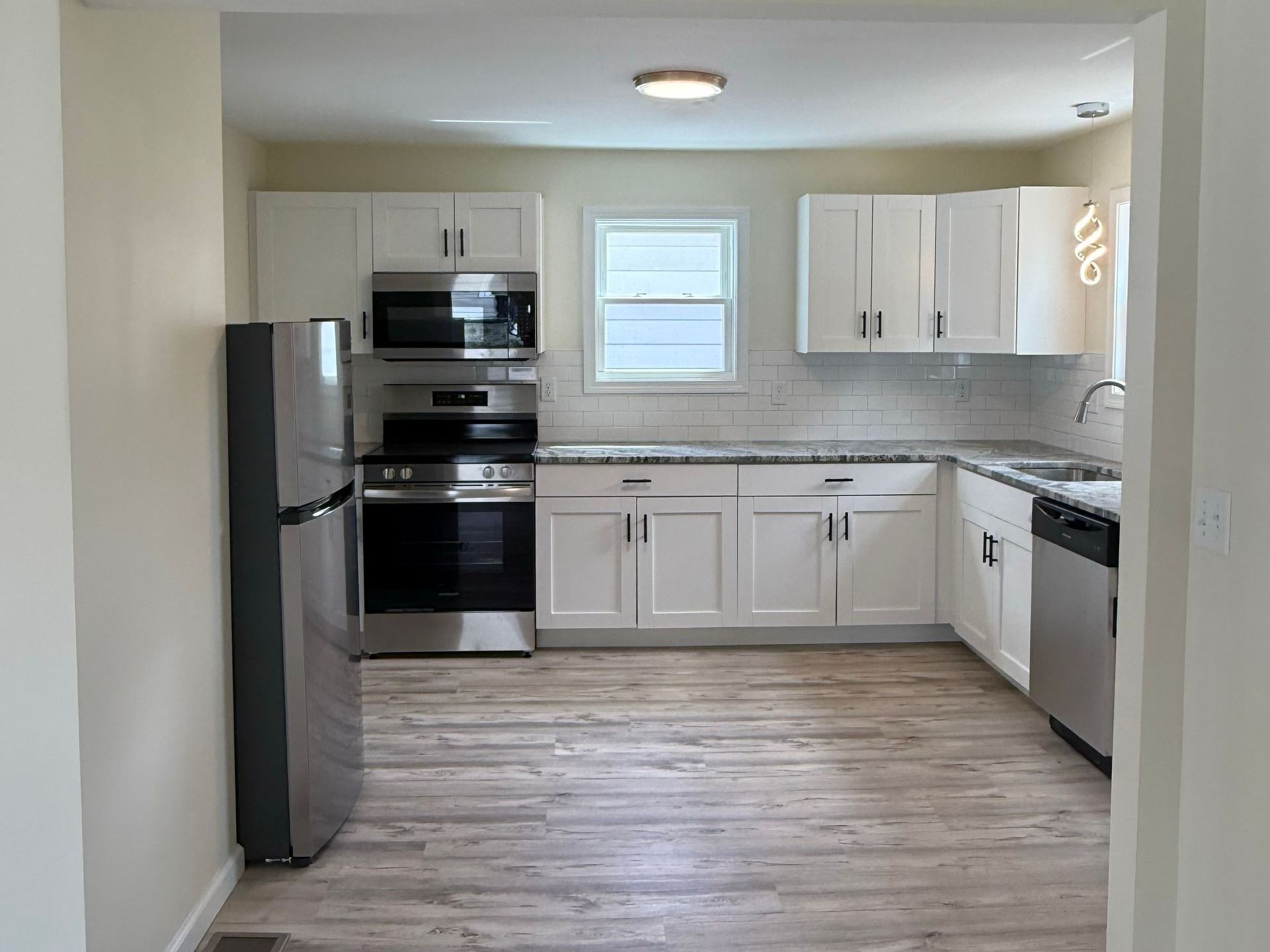 Modern kitchen with white cabinets, stainless steel appliances, and light gray countertops. The room has light wood-look flooring.