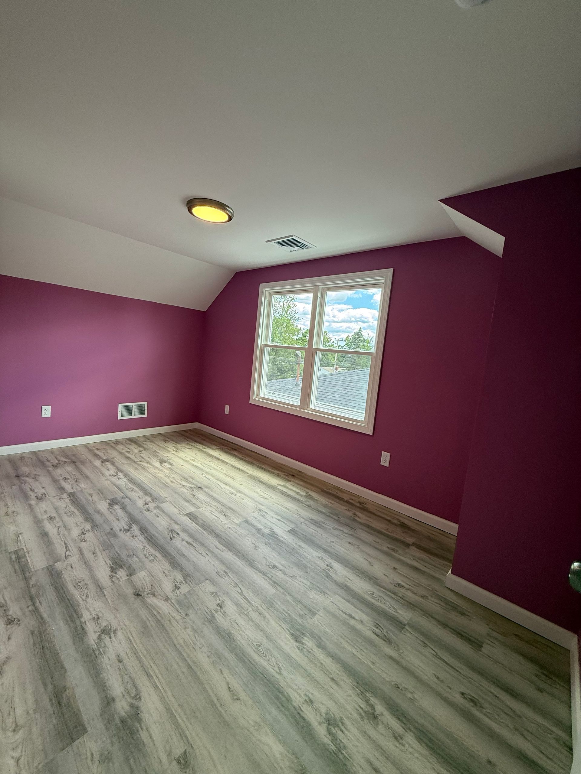 Bedroom with purple walls, white trim, a window, and gray wood-look flooring.