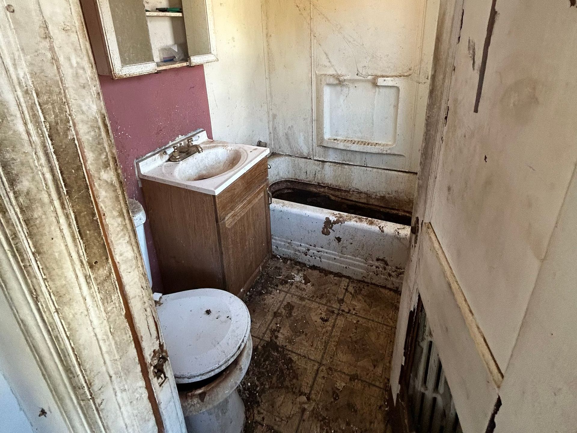 A dilapidated bathroom with a dirty toilet, sink, and bathtub. The walls are stained and peeling.