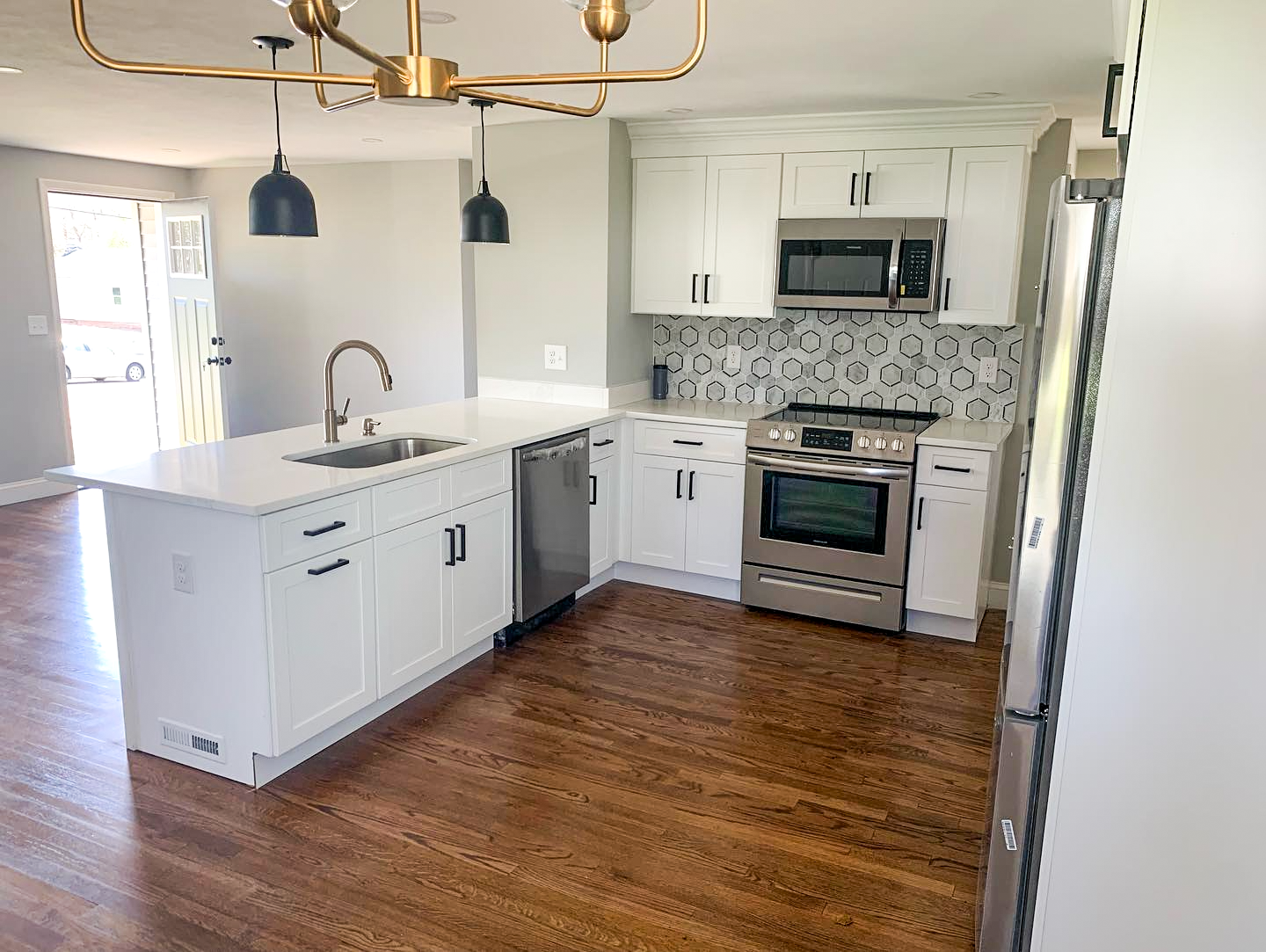A kitchen with white cabinets , stainless steel appliances , hardwood floors and a large island.