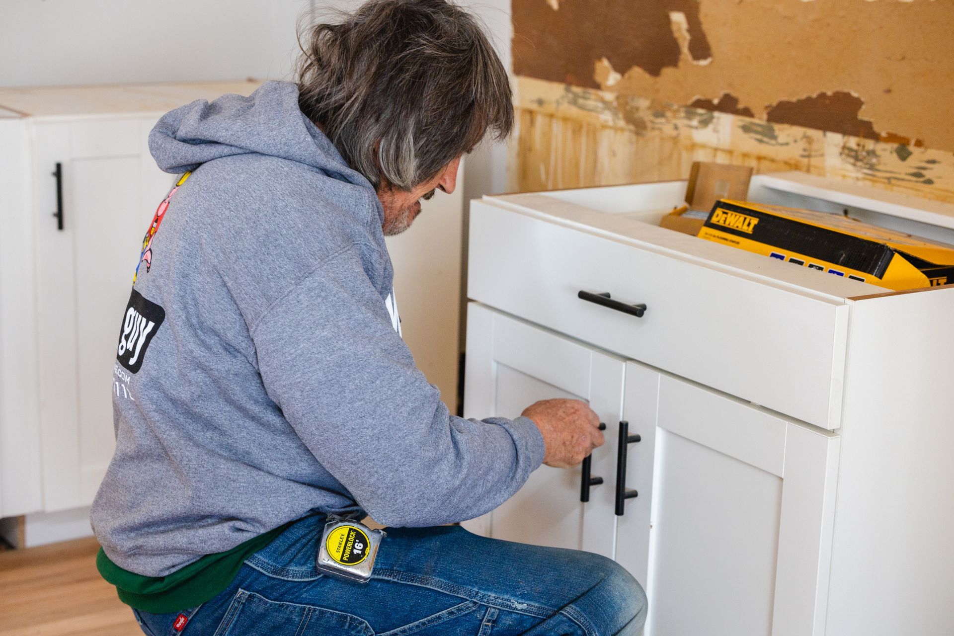 A man is kneeling down and working on a cabinet.