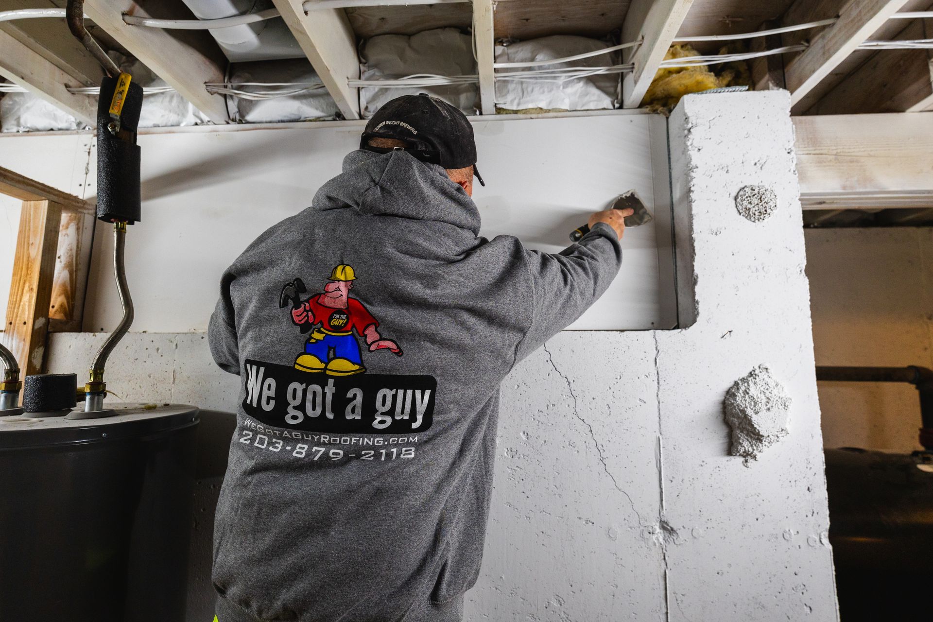 A man wearing a We Got a Guy sweatshirt is working on a wall.