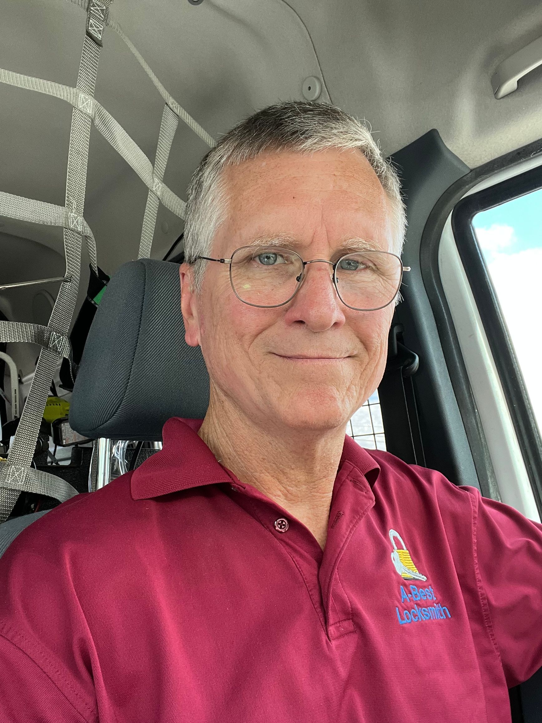 A man wearing glasses and a red shirt is sitting in a car.