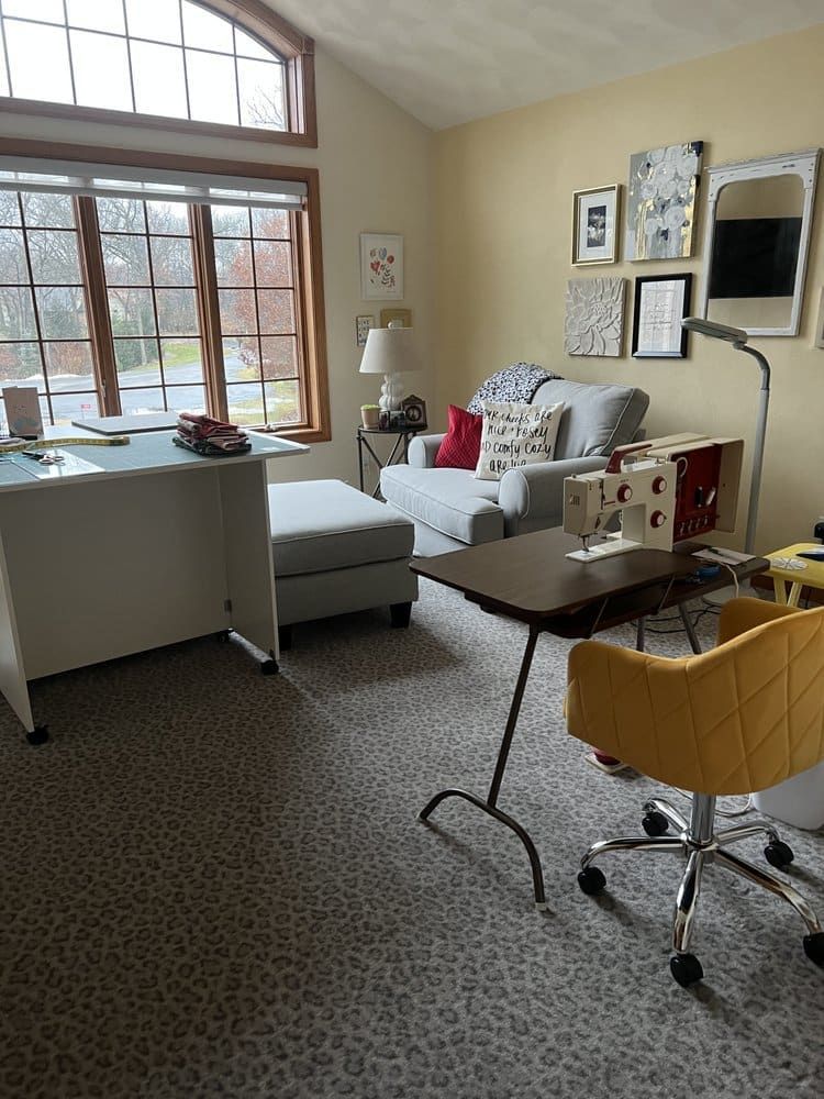 A living room with a sewing machine, desk, chair and couch.