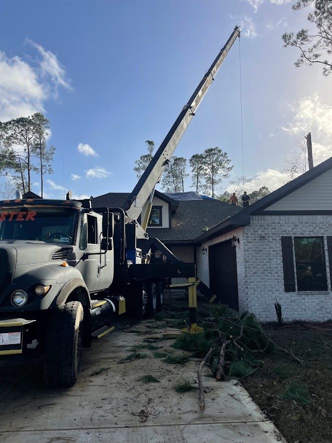 A crane is cutting down a tree in a yard.