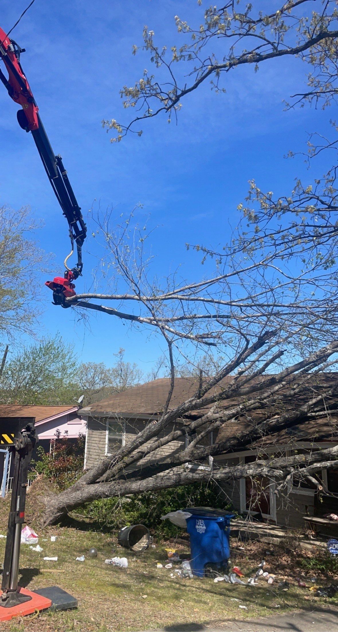 A crane is cutting down a tree in a yard.