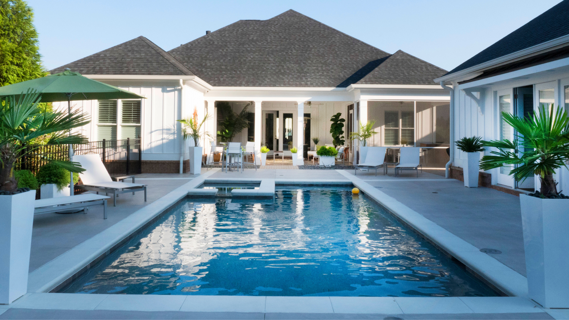 Modern white villa with a central blue swimming pool and lounge chairs on the patio