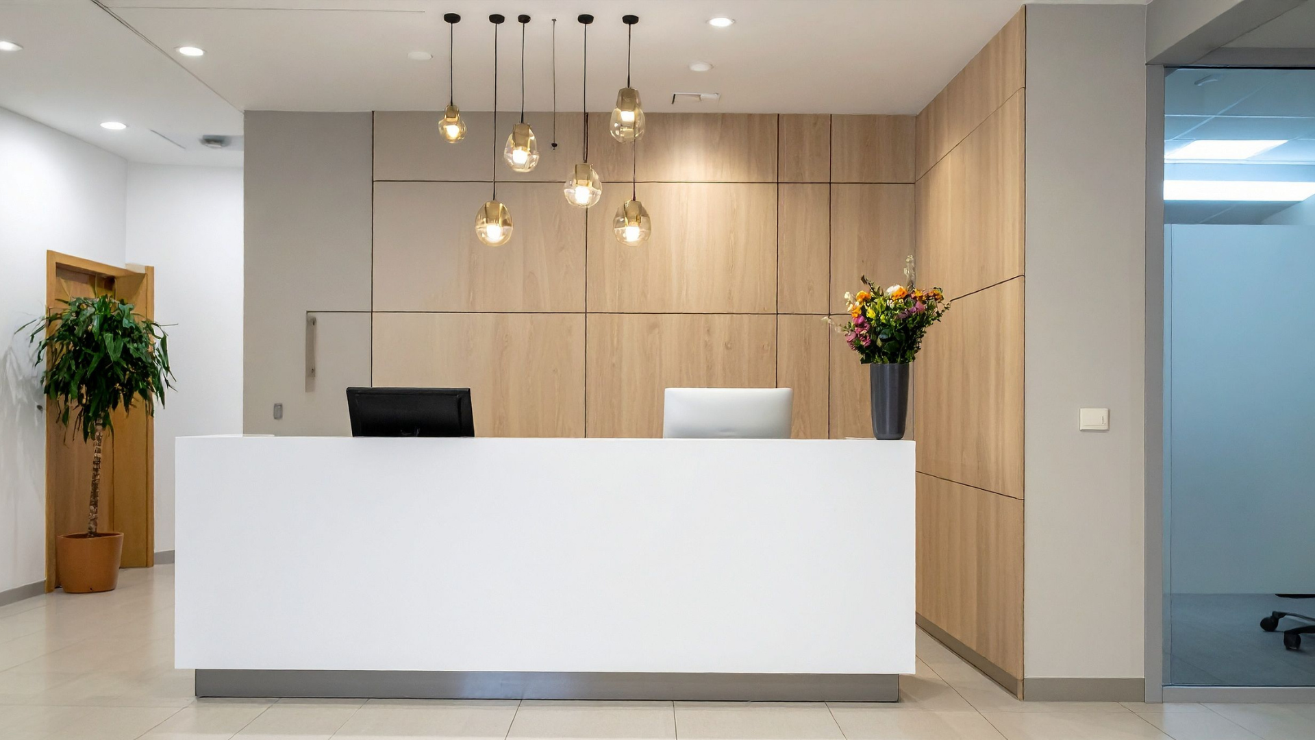 Modern office reception desk with wood-paneled wall, pendant lights, and a potted plant