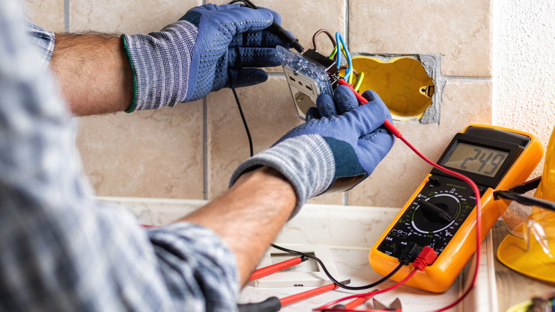Person installing electrical wiring in a wall outlet with a multimeter nearby
