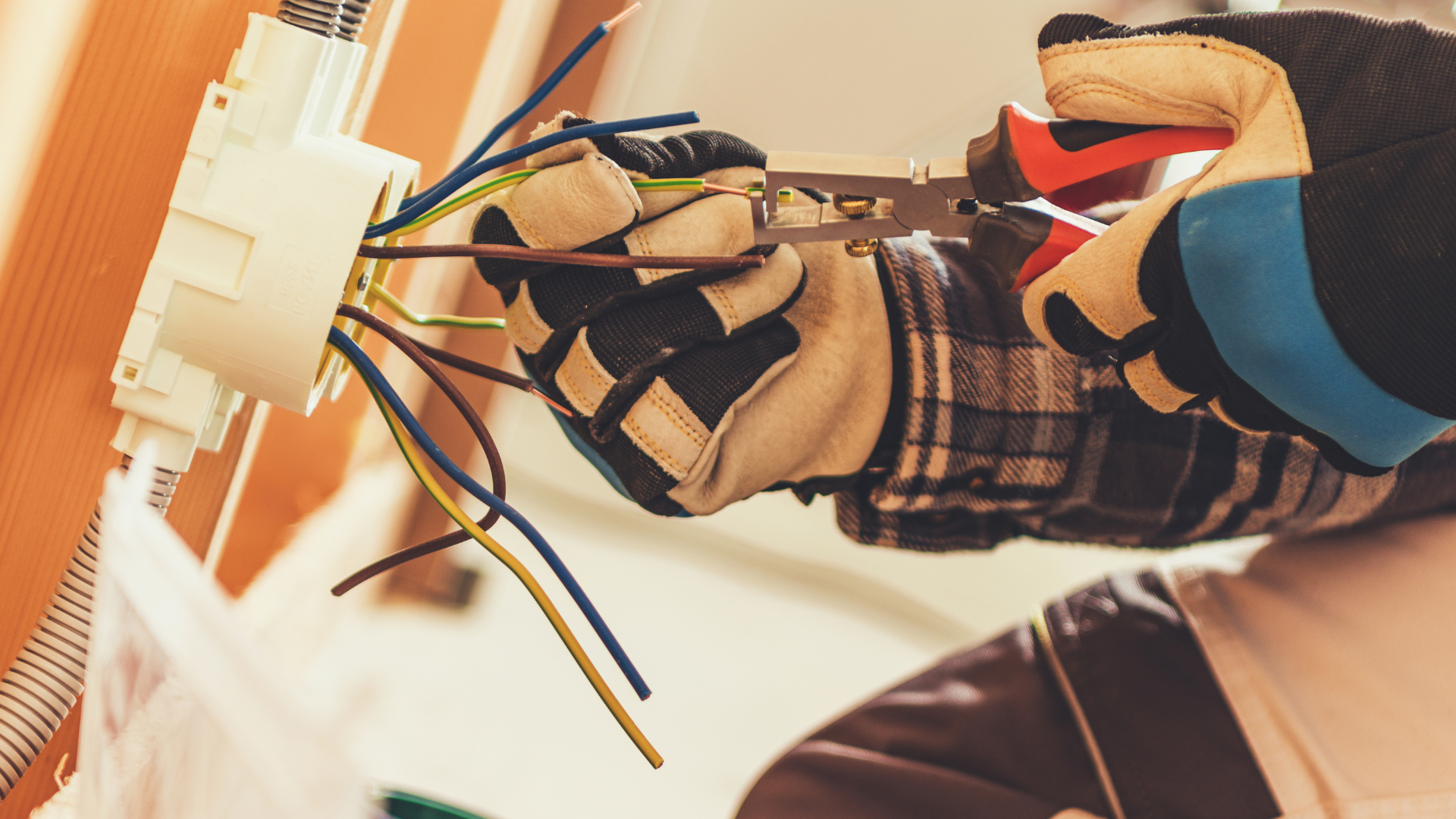 Gloved hands working on exposed electrical wires inside a wall switch box