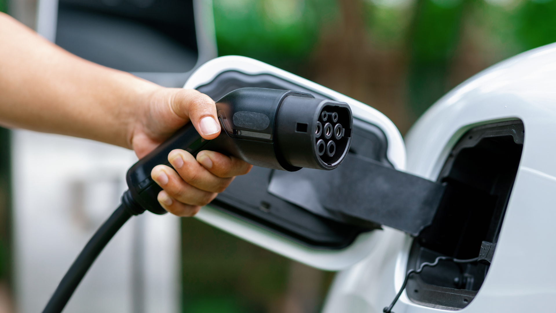 Hand plugging an EV charging connector into a car’s charging port