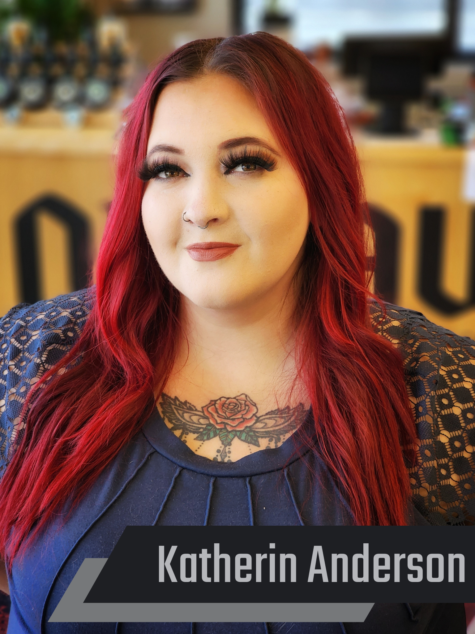 A woman with red hair is wearing a blue shirt and has a tattoo on her chest.