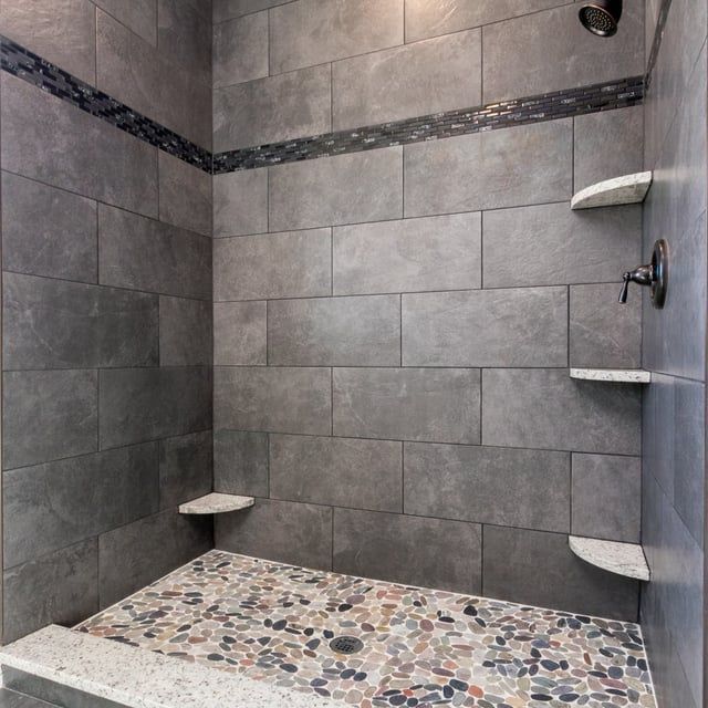 A shower with gray tiles and a pebble floor