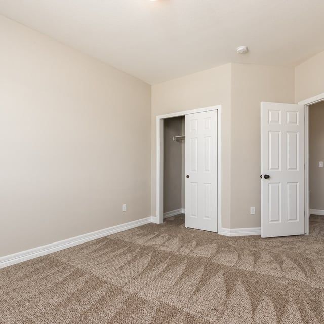 An empty bedroom with a carpeted floor and two doors.