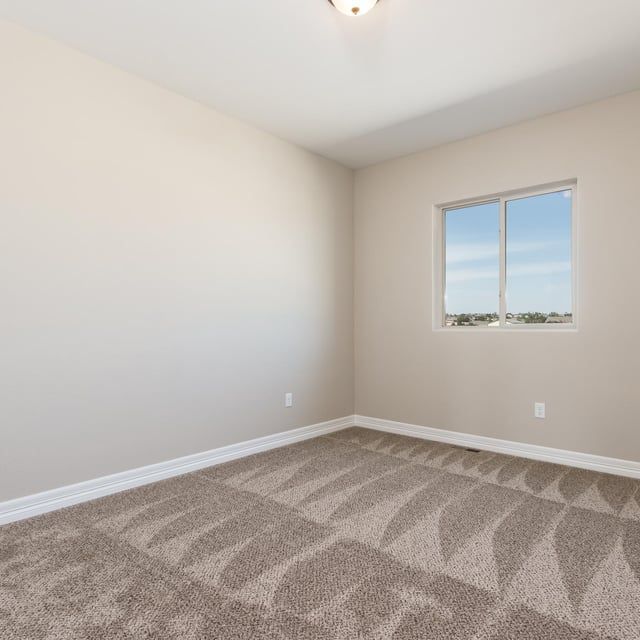 An empty bedroom with a window and a carpeted floor
