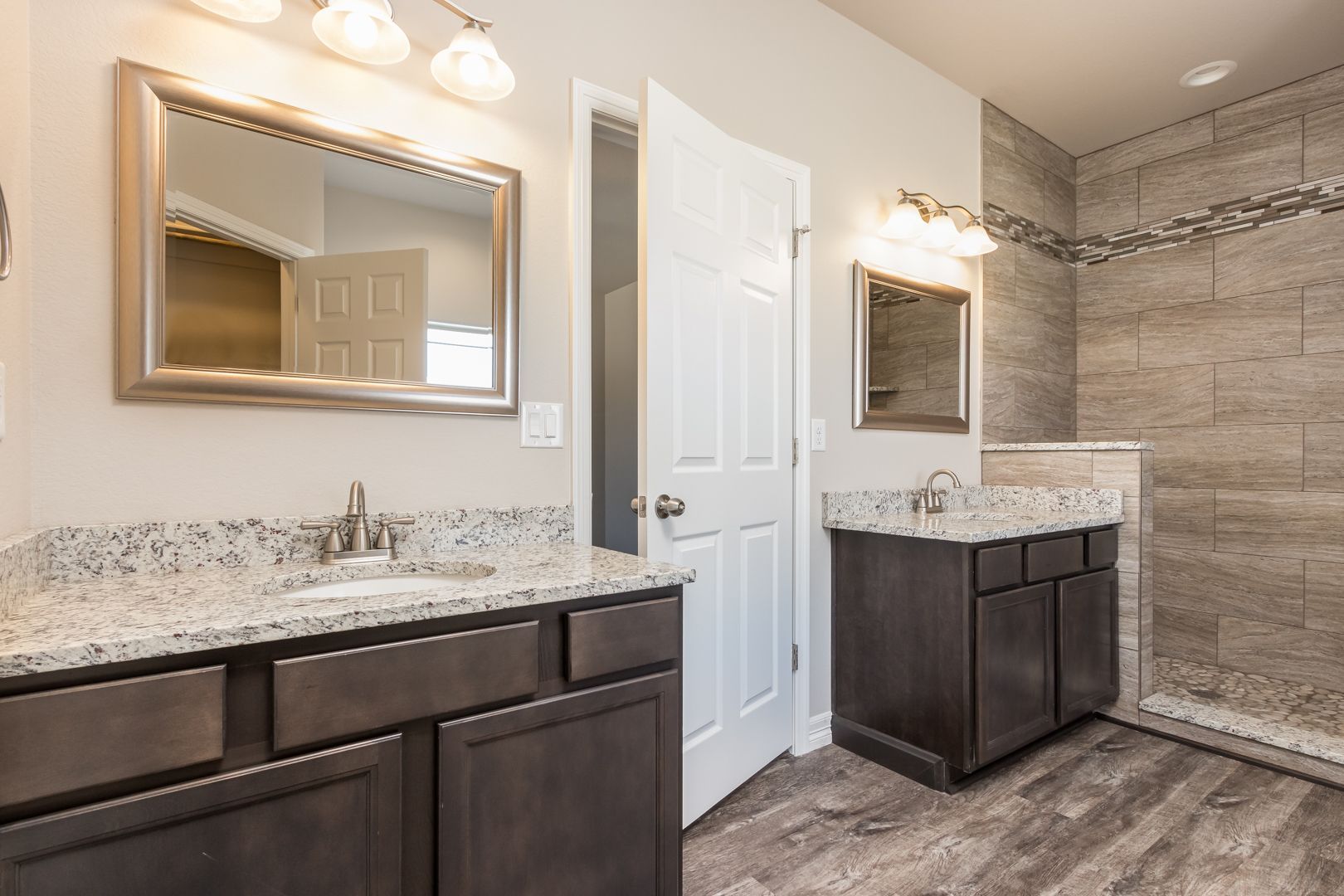 A bathroom with two sinks , two mirrors and a walk in shower.