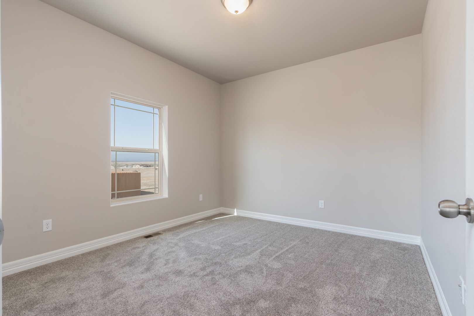 An empty bedroom with a window and a carpeted floor.