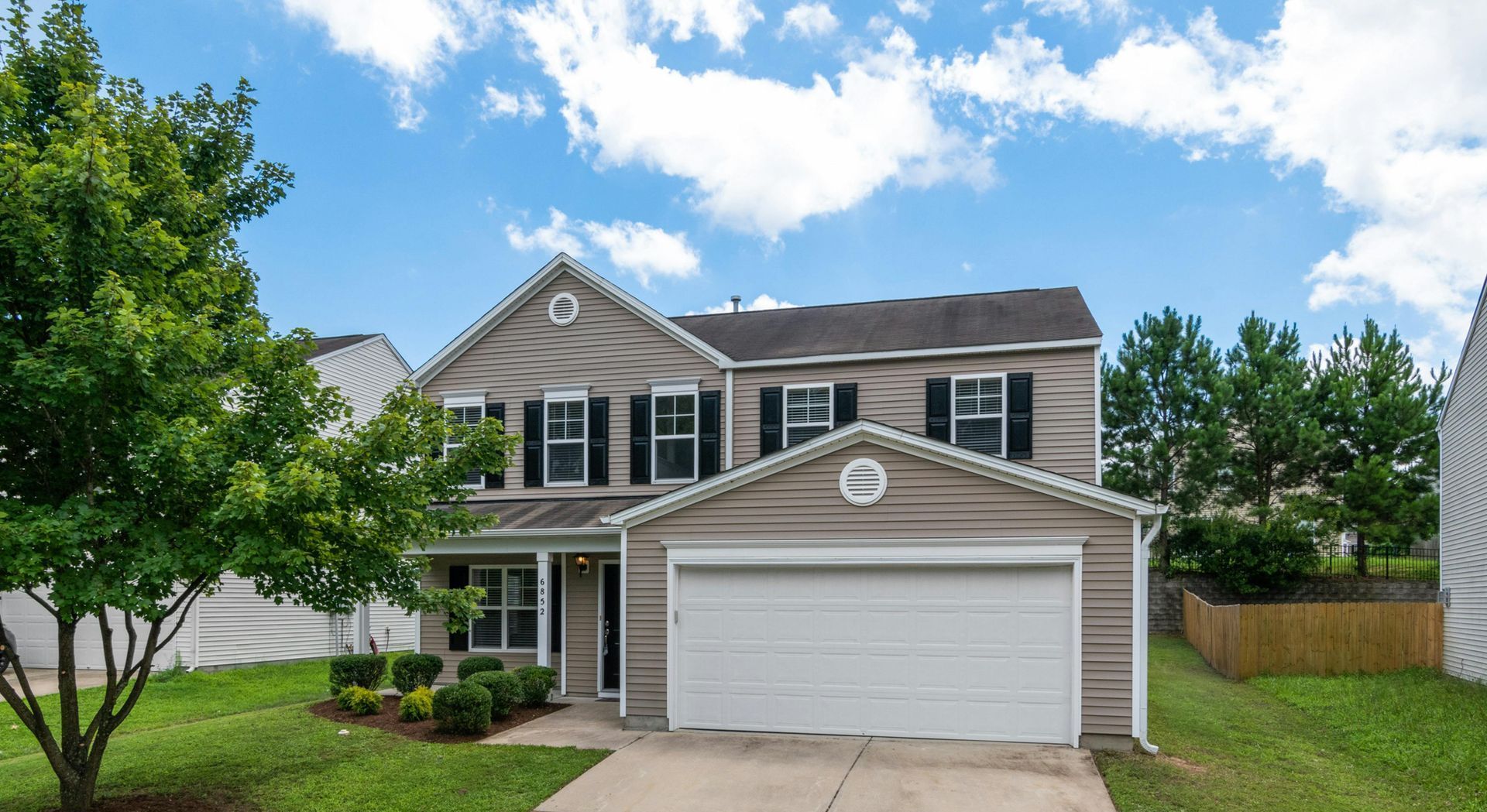 A large house with a white garage door and a tree in front of it.