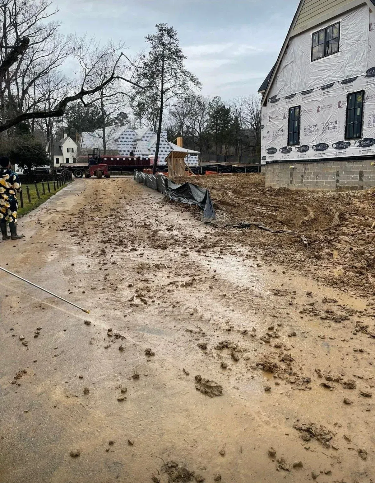 A muddy construction site in front of a house under renovation with a person standing on the left side of a dirt road.